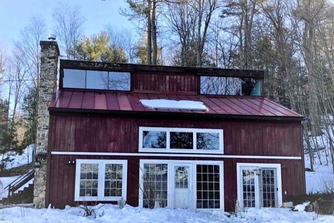 The home before, with faded red board-and-batten siding and a stone chimney